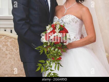 Sposa e sposo in un abito da sposa bianco contiene un bouquet di bellissimi fiori di rose bianche e rosse, primo piano. Foto Stock