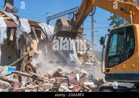 Processo di demolizione di vecchi edifici. Casa di rottura dell'escavatore. Distruzione di alloggi fatiscenti per un nuovo sviluppo. Foto Stock