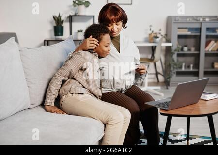 Ritratto di donna afro-americana incinta abbracciando il figlio mentre si siede sul divano a casa, spazio di copia Foto Stock