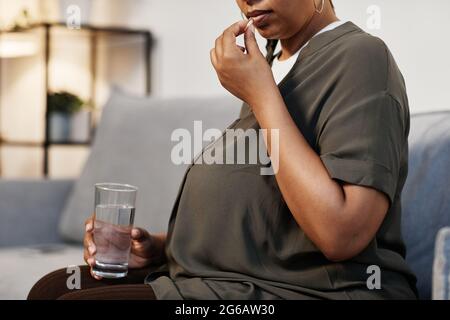 Vista laterale ritratto di donna afroamericana incinta prendendo vitamine prenatali a casa, copia spazio Foto Stock