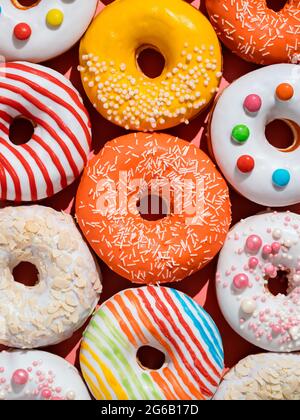 Ciambelle colorate assortite con spruzzi. Layout creativo realizzato con deliziose ciambelle smaltate. Sfondo piatto verticale con ciambelle o ciambelle multicolore Foto Stock