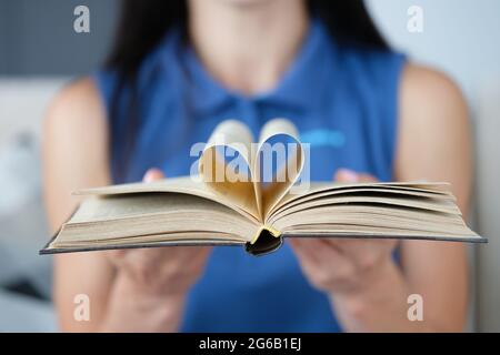 La donna sta tenendo il libro con una pagina in forma di cuore piegato nel centro Foto Stock