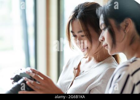 Felici le donne asiatiche affascinanti stanno controllando e guardando la loro immagine sullo schermo LCD della fotocamera dopo la ripresa. Foto Stock