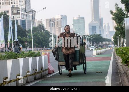 Un venditore di strada tira il carrello su una strada vuota durante l'imposizione delle restrizioni di emergenza. L'Indonesia ha imposto restrizioni alle attività comunitarie di emergenza, localmente note come PPKM, a Java e Bali dal luglio 3-20 per frenare l'epidemia di Covid-19 del paese dopo che la precedente politica di micro PPKM si è rivelata inefficace. Il Ministero della Salute ha detto sabato che l'Indonesia ha registrato 27, 913 casi recentemente confermati di Covid-19 nelle ultime 24 ore, il picco più alto giornaliero, portando il totale a 2, 256, 851, dal momento che il primo caso è stato rilevato nel marzo 2020. (Foto di Agung Fatma Putra/SOPA im Foto Stock