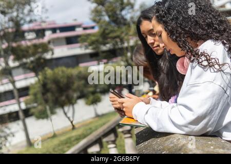 Due studenti di Girlfriends ispanici teen interagiscono con un cellulare su una terrazza Foto Stock