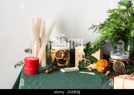 Tavolo festoso decorato Natale o Capodanno, rami thuja e abete rosso, candele e fette di agrumi secchi, biscotti al cioccolato in un vaso Foto Stock