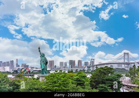 tokyo, giappone - luglio 18 2020: Statua della libertà che sorge sul parco della spiaggia di Odaiba con il monumento degli anelli Olimpici portato su una chiatta che galleggia sulla Baia di Odaiba Foto Stock