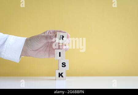 Mano accatastare su cubi di legno per rendere la parola, rischio. Su sfondo giallo, con spazio per la copia. Foto Stock