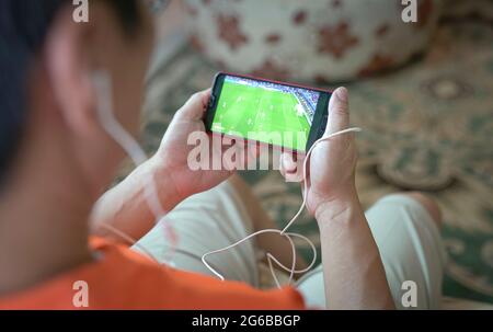 Uomo che guarda il calcio e lo sport in streaming sul dispositivo smartphone. Home sfondo interno. Foto Stock
