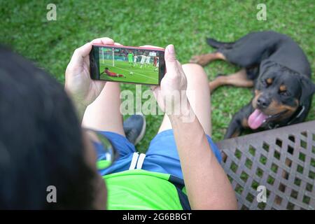 Uomo che guarda il calcio e lo sport in streaming sul telefono cellulare con il cane accanto. Concetto di Home Entertainment. Foto Stock