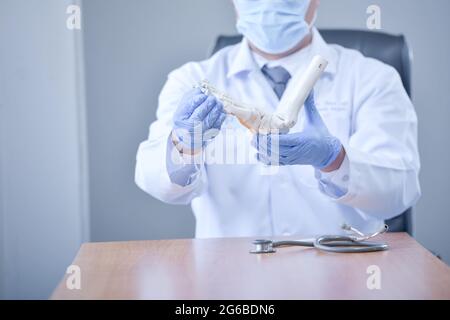 Medico che indossa una maschera facciale che tiene un osso artificiale del piede Foto Stock