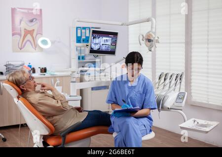 Assistente nel gabinetto dentista durante la donna anziana igiene orale controllare seduta su sedia. Donna anziana che parla con l'infermiera medica in ufficio di stomatologia circa il problema dei denti. Foto Stock