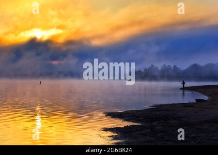 Pesca della canna al lago Jindabyne sul fiume Snowy in Australia - cols mattina nebby con il sole che sorge. Foto Stock