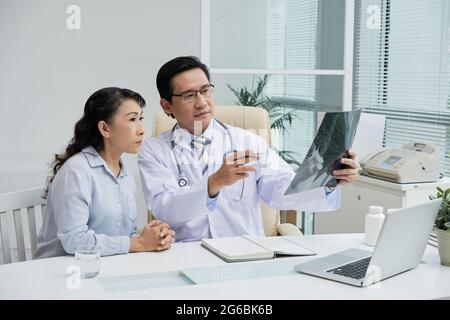 Medico che mostra l'immagine radiografica del paziente anziano quando è seduto al tavolo Foto Stock