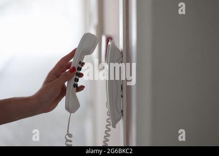 Donna mano che raccoglie il telefono nel corridoio dell'hotel vicino Foto Stock