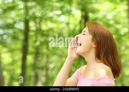 Vista laterale ritratto di una donna che grida forte in una foresta Foto Stock