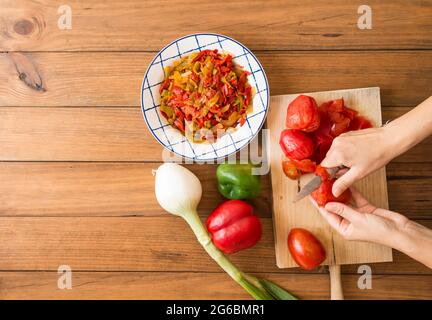 Dettaglio delle mani di una donna che spellano i pomodori con un coltello. Preparazione di peperoni arrostiti, un piatto tipico della cucina spagnola e andalusa. Foto Stock