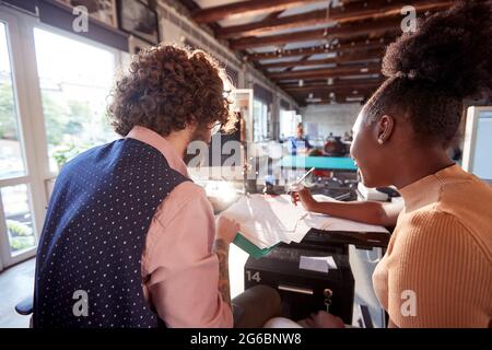 Due giovani colleghi stanno passando alcuni documenti al lavoro in un'atmosfera piacevole in ufficio Foto Stock