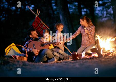 Una giovane e felice famiglia che ha giocato intorno a un falò nella foresta in una bella notte Foto Stock