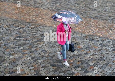 05 luglio 2021, bassa Sassonia, Osnabrück: Una donna cammina con un ombrello su una piazza con ciottoli. Con temperature intorno a 15 gradi e pioggia in parte pesante il tempo è poco amichevole in molte parti della bassa Sassonia. Foto: Frito Gentsch/dpa Foto Stock