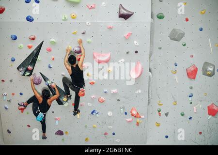 Giovani atleti allenarsi al chiuso e arrampicarsi sulla parete di bouldering, vista dall'alto Foto Stock