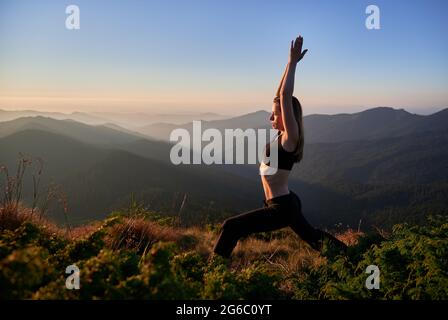 Vista laterale della donna slim in nero sportivo che si allunga sulla natura. Concetto di armonia con la libertà e la natura. Foto Stock