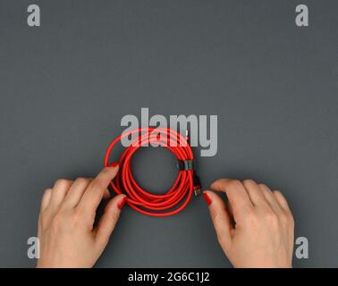 la mano femmina tiene il cavo ritorto per caricare i dispositivi mobili in un involucro di tessuto rosso su uno sfondo nero, primo piano Foto Stock
