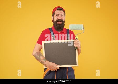 Pronto al lavoro. Idea creativa. Caposquadra pubblicizza il servizio di parete di fronte. Uomo felice con spazio di copia del bordo. Hipster maturo uso strumento rullo di vernice per Foto Stock