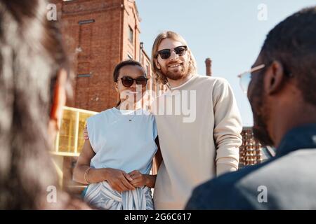 Vita ritratto di giovane coppia contemporanea incontrare amici all'aperto in città, entrambi indossando occhiali da sole Foto Stock