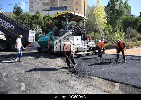 I lavoratori stranieri palestinesi che indossano giubbotti protettivi sparse l'asfalto posato dalla Asphalt Paver Finisher, ha posato il primo livello sulla strada spazzata. Foto Stock