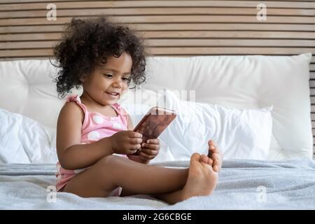 Carino scalfetto afroamericano ragazza poco divertente giocare con il telefono cellulare Foto Stock