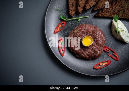 vista dall'alto della tartare di bistecca di manzo con tuorlo d'uovo crudo sul piatto su sfondo nero Foto Stock