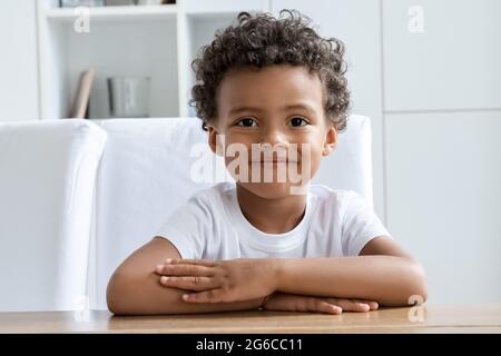 Carino felice sorridente bambino studente preschool seduto alla scrivania guardando la macchina fotografica Foto Stock
