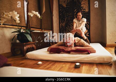 Un maschio maturo che gode di un massaggio di riabilitazione in studio orientale Foto Stock