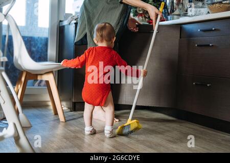 Piccole madri aiutate. Carino bambino ragazza con la mop aiutare la sua mamma fare casalinghi in cucina. Carino bambina giocare con mop e fa la pulizia Foto Stock