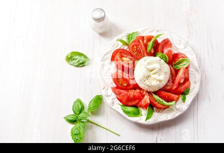 Insalata burrata su piatto bianco. Vista dall'alto dell'insalata con burrata e foglie di basilico su tavola bianca. Foto Stock