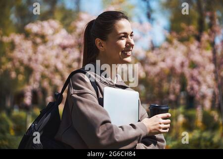 Studente che cammina all'esterno con zaino e computer portatile Foto Stock