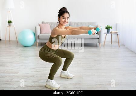 Forte giovane donna indiana che lavora con manubri, squatting a casa, spazio vuoto Foto Stock