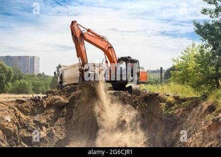 escavatore cingolato arancione e dumper da cantiere in fase di scavo. Preparazione del sito. Carico e trasporto di suolo Foto Stock