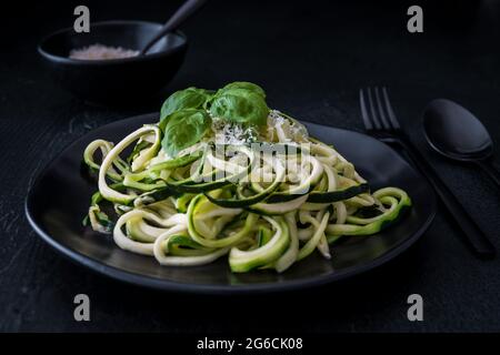 Zoodles, spaghetti di zucchine con parmigiano e basilico su un piatto nero su fondo nero. Per basso contenuto di carboidrati, keto, vegetariani, paleo, alimentazione e dieta. Foto Stock