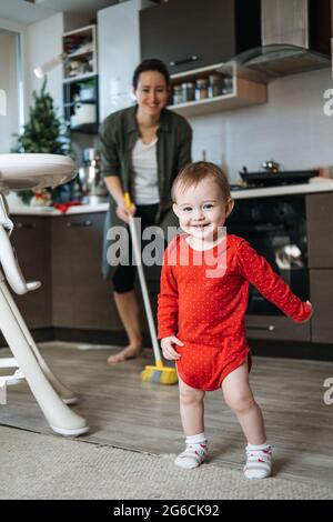 Piccole madri aiutate. Carino bambino ragazza con la mop aiutare la sua mamma fare casalinghi in cucina. Carino bambina giocare con mop e fa la pulizia Foto Stock