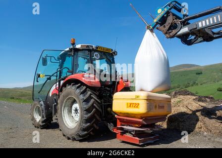 Caricamento di un spandiconcime con un fertilizzante granulare NPK 20-10-10 da distribuire su terreni in salita per favorire la crescita dell'erba. Foto Stock