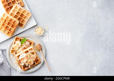 Waffle belgi con banana, caramello e crema su sfondo grigio in cemento, vista dall'alto, spazio per fotocopie Foto Stock