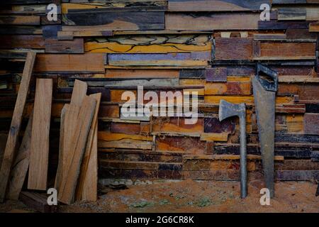 L'ascia e la sega a mano in metallo che poggiano contro vecchie pareti sono fatte di diversi tipi di legno Foto Stock