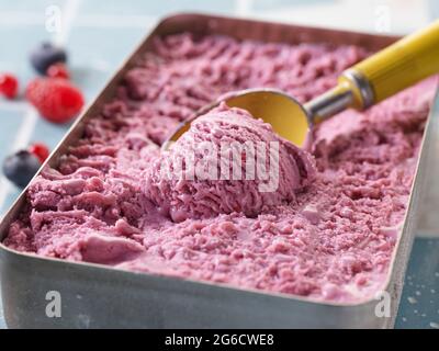 Primo piano di delizioso gelato fatto in casa con frutti di bosco misti in contenitore con cucchiaio Foto Stock