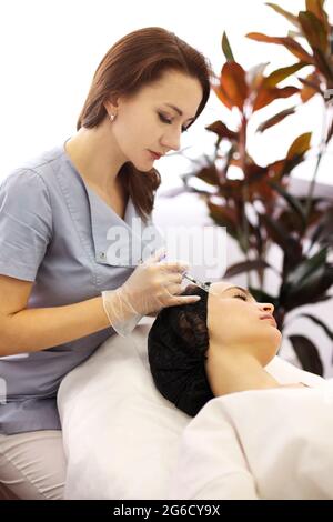 Estetista professionista che inietta acido ialuronico vicino agli occhi della donna durante procedura anti invecchiamento in clinica di bellezza Foto Stock