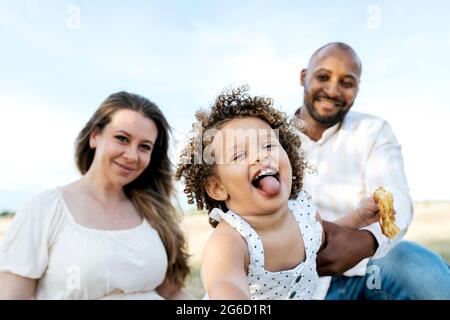 Felice famiglia multietnica con carina piccola figlia godendo pic-nic estivo in natura Foto Stock