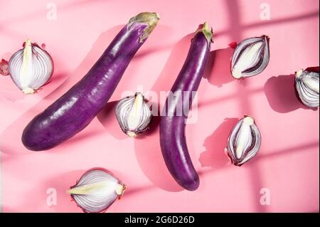 Vista dall'alto composizione di natura morta con melanzane intere fresche e bulbi a cipolla rossa a metà posti su sfondo rosa con luce e ombre Foto Stock