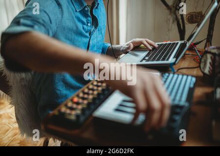 Vista laterale di un giovane uomo dal taglio irriconoscibile che lavora sul sintetizzatore e sul laptop a casa Foto Stock