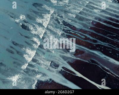 Dall'alto si può ammirare un paesaggio dall'alto con una ruvida costa rocciosa irregolare e onde dell'oceano schiumose con ruscelli Foto Stock